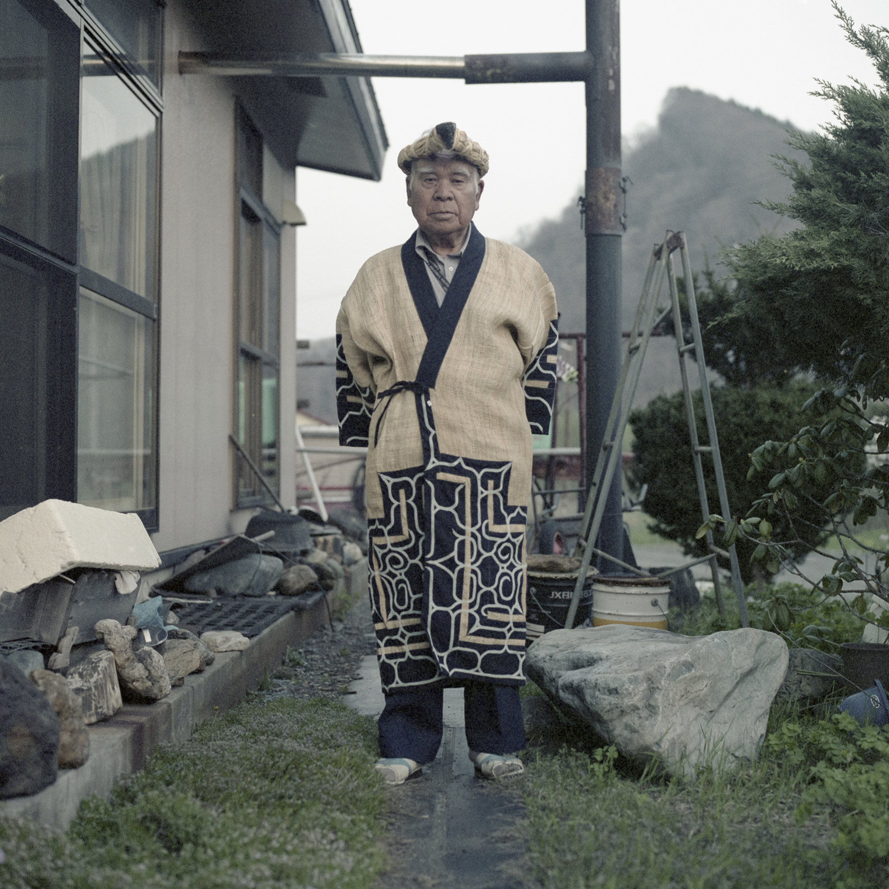 Nibutani, Hokkaido, Japan 2015 
Kazunobu Kawanano is a proud Ainu Ekashi (elder) and an active member of the local Ainu community. He is pictured in front of his home, wearing a traditional Attush robe his wife Motoko weaved for him.