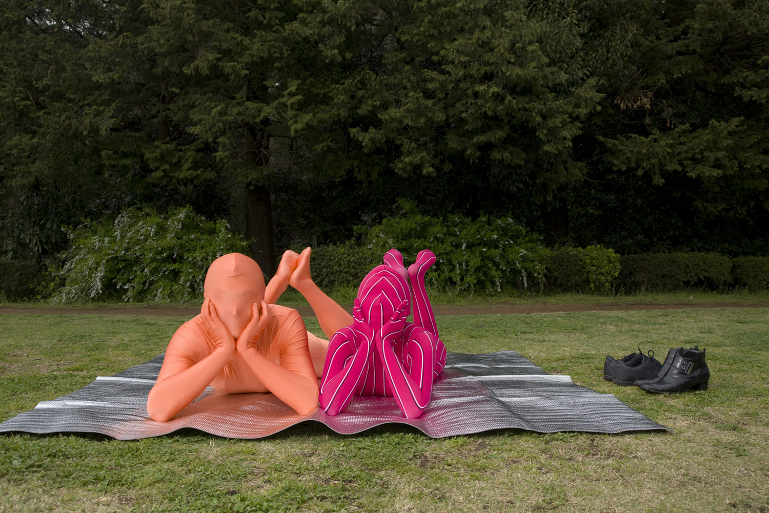 Kawasaki, Greater Tokyo. Rawen (left) 56, office worker and his partner Mii (right) 55, office worker, wear Zentai suits on a pic nic mat at a local park.