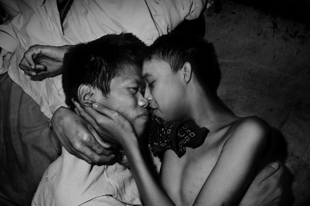 Two male teenagers comforting eachother inside the main room of a Filipino psychiatric hospital.