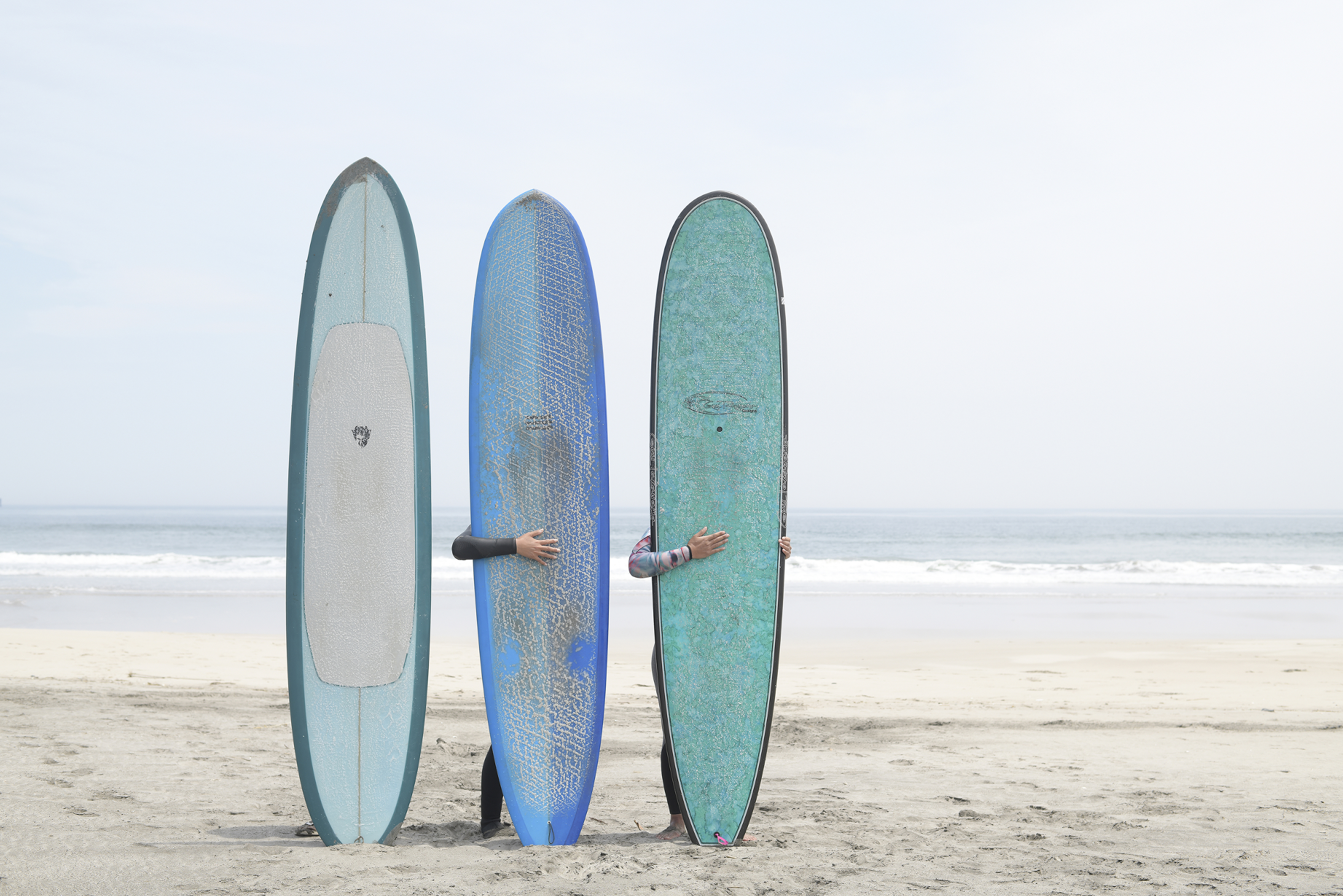 Kitaizumi Beach, Minamisoma, Fukushima Prefecture, Japan. Three surfers pose for a portrait behind their longboards on the beach.
