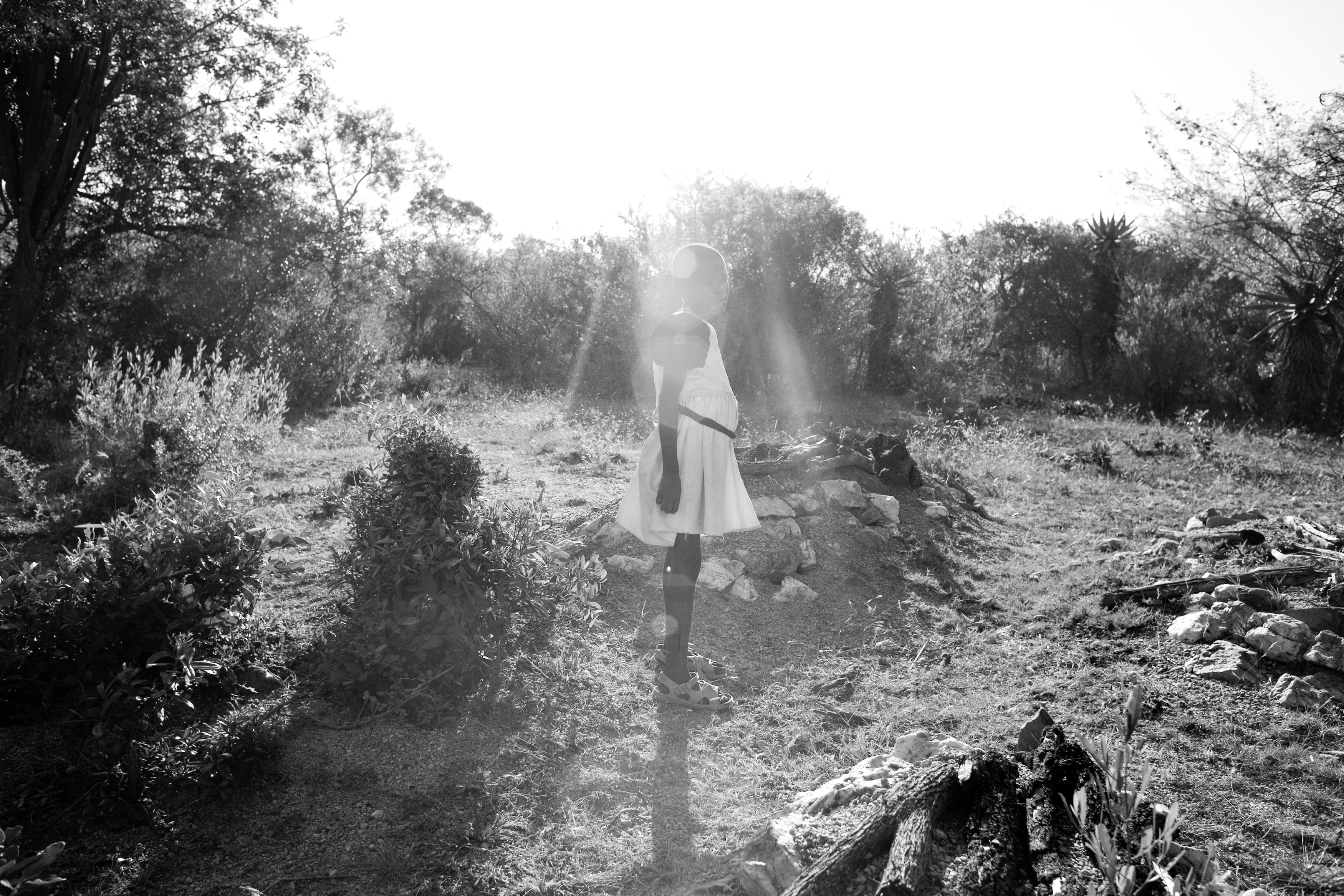An HIV positive girl, 12, stands near the grave of her father at the family burial ground near their rural home. She has lost both of her parents to AIDS and is now cared for by her HIV positive aunt along with her brother and cousin. She often collects fire wood around the site where many of her extended family are buried.